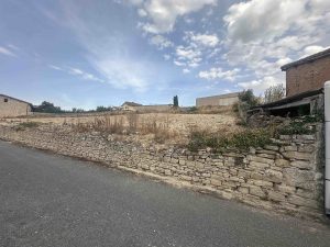 Terreno residencial en Armiñón, Álava, visto desde la calle, con muro de piedra y parcela elevada sin edificar.