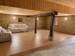Txoko reformado con paredes de piedra vista, vigas de madera y zona de estar